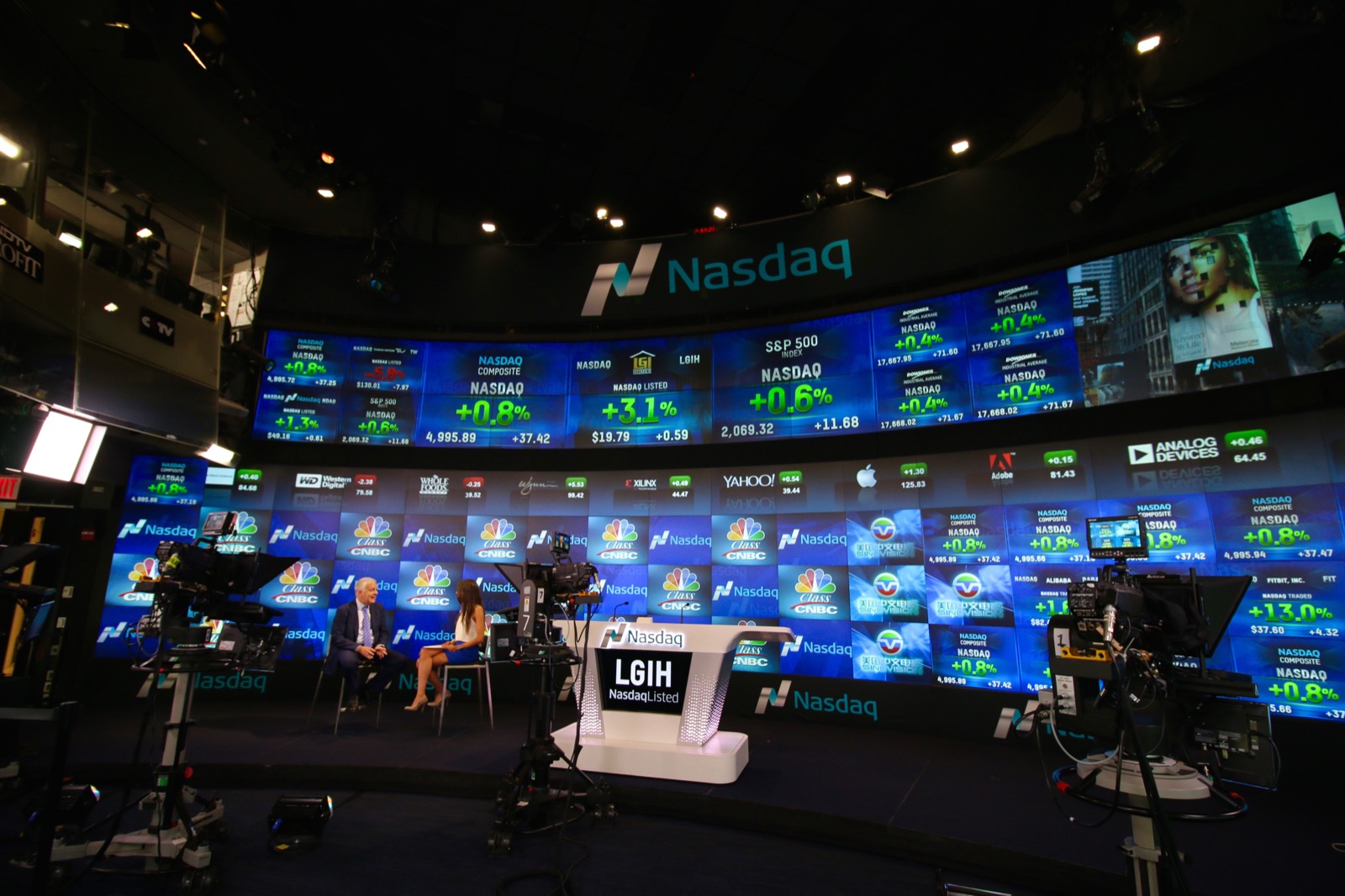 The curved video wall of the Nasdaq MarketSite studio in New York, with a broadcast desk and cameras in front