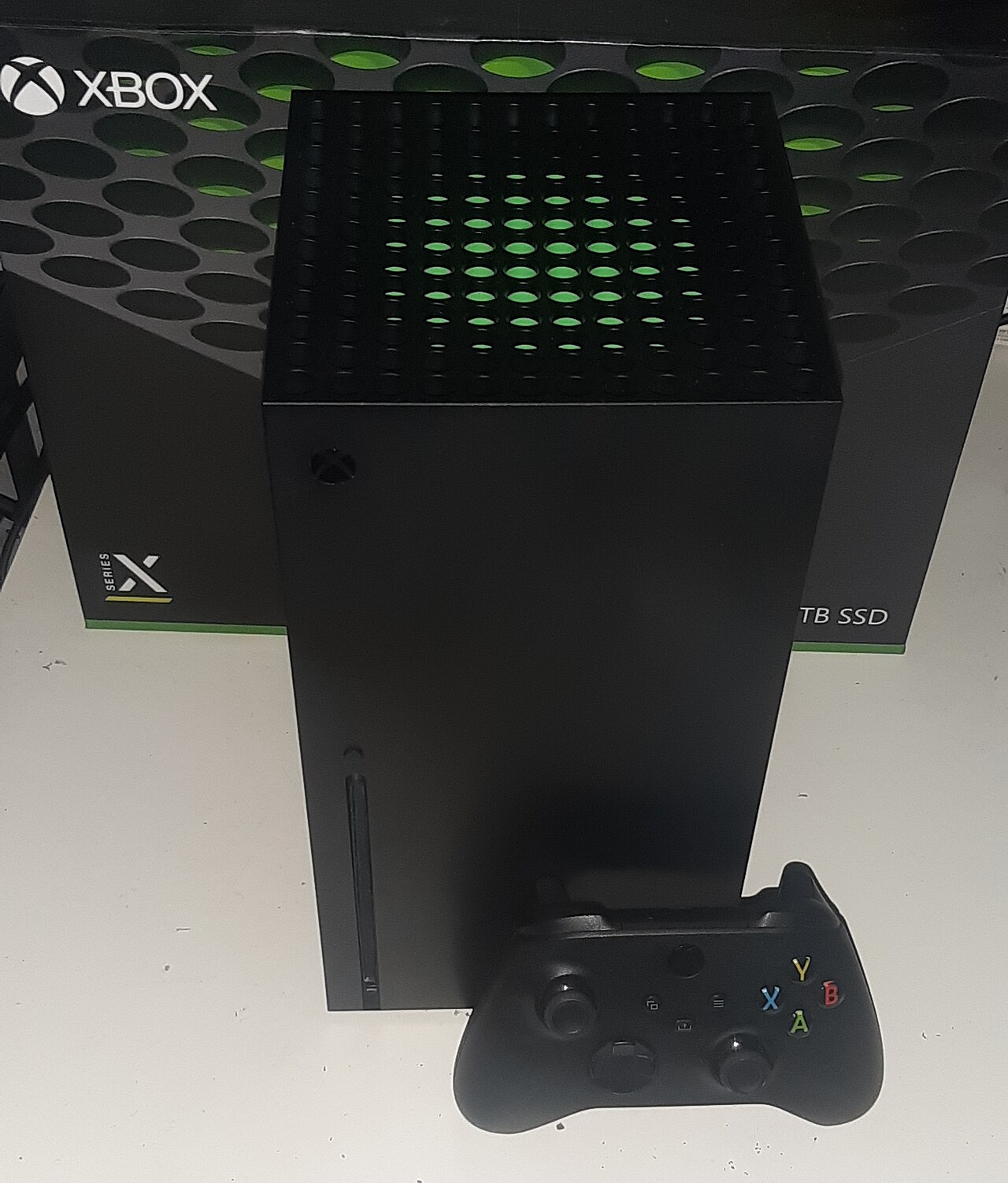 A Microsoft Xbox Series X console standing upright beside its controller