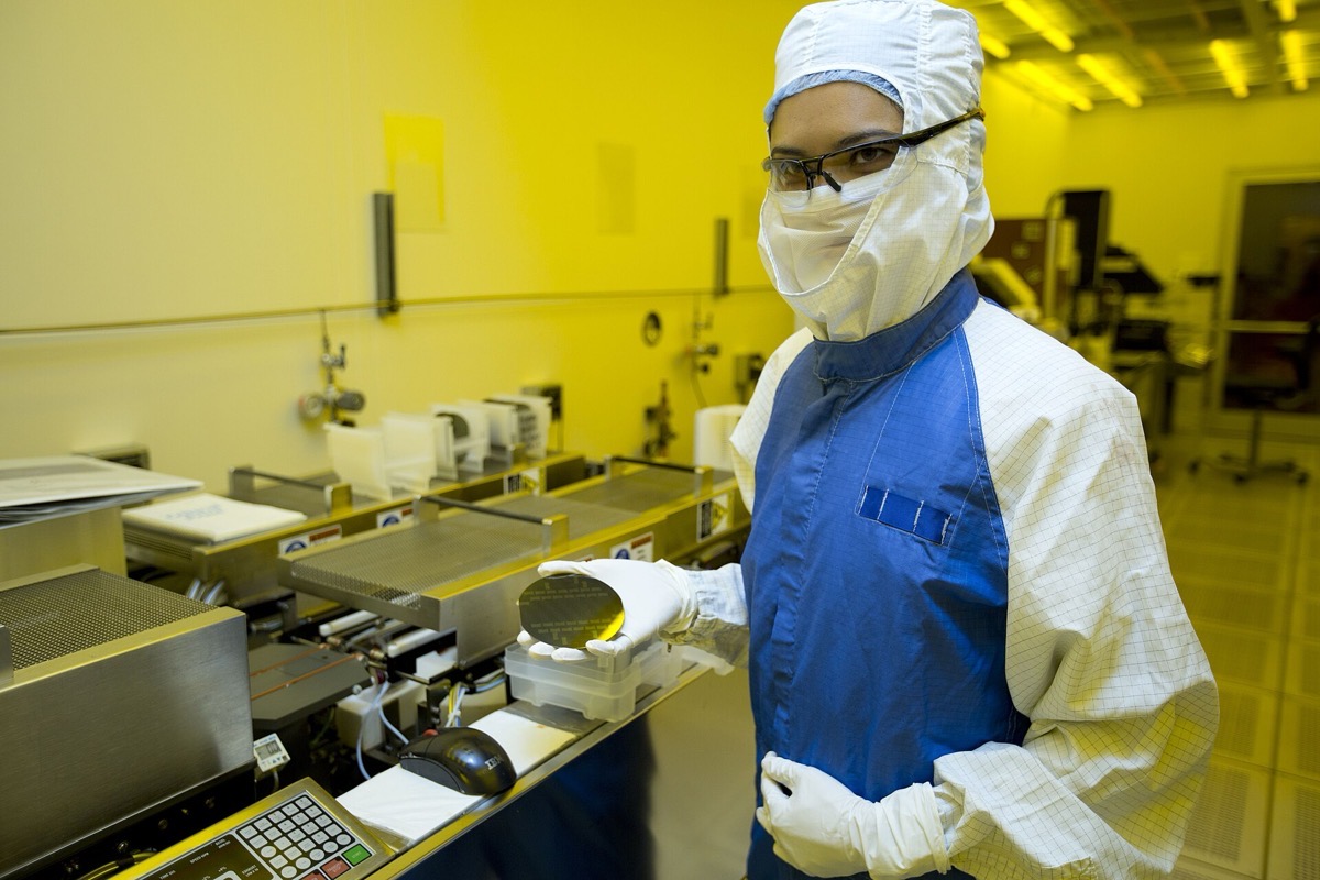 A researcher holding a silicon wafer being removed from processing equipment