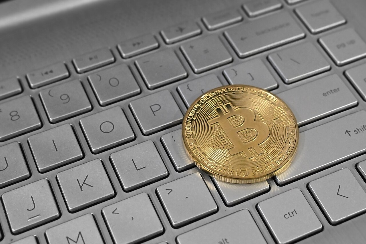 A physical bitcoin coin resting on the keys of a laptop keyboard